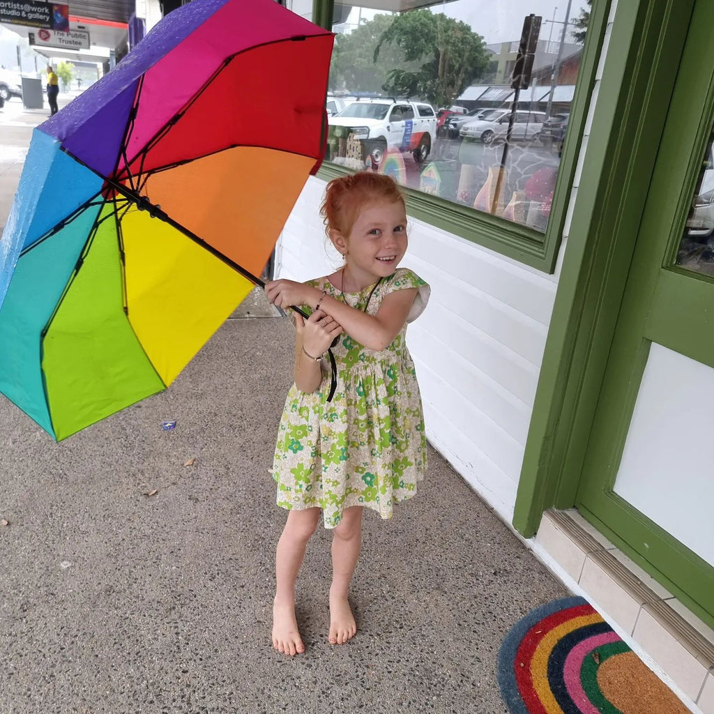 young girl holding large compact automatic rainbow umnbrella outside Earth Toys on Sheridan St Cairns